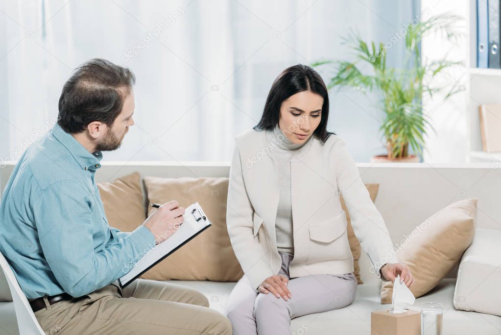 upset young woman holding paper tissue during therapy session with psychiatrist