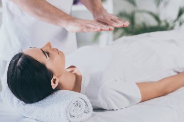 Masaj masanın üzerinde yatan ve reiki tedavi gören genç kadın