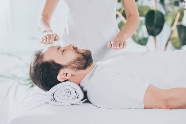 cropped shot of calm bearded man with closed eyes receiving reiki healing therapy clipart