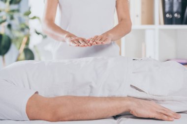 cropped shot of man lying on massage table and receiving reiki treatment clipart
