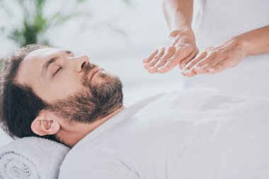cropped shot of calm bearded man with closed eyes receiving reiki treatment  clipart