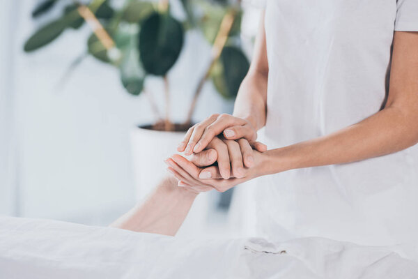cropped shot of reiki healer holding hand of male hand