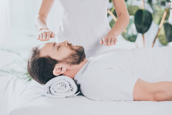 cropped shot of calm bearded man with closed eyes receiving reiki healing therapy