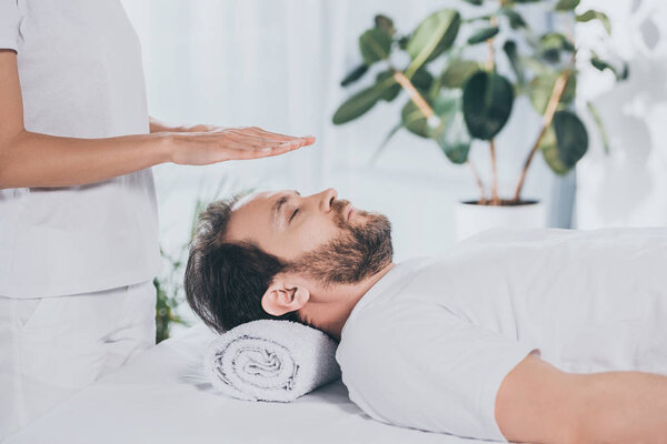 calm bearded man with closed eyes receiving reiki treatment above head   