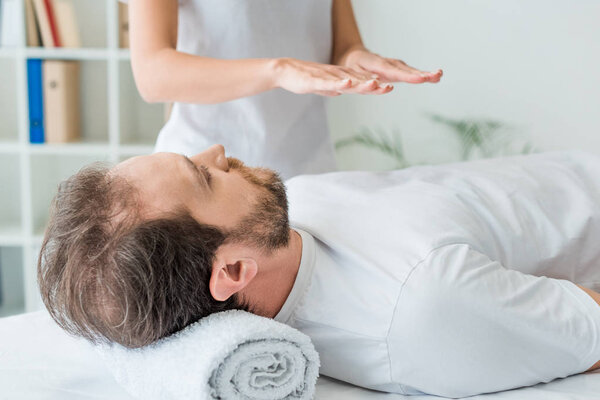 cropped shot of bearded man lying on massage table and receiving reiki treatment 