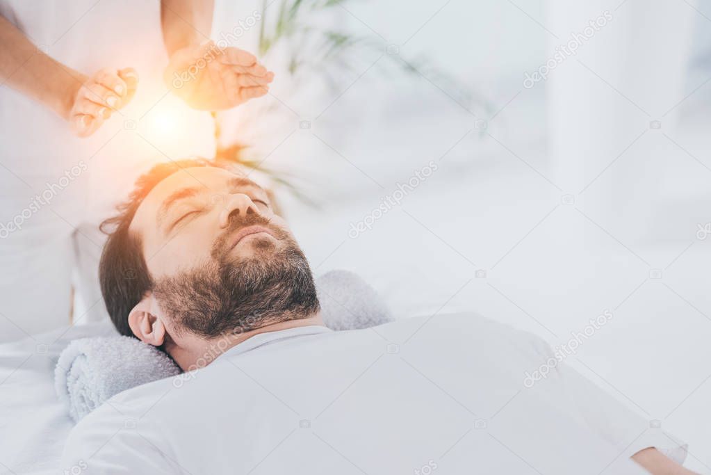 calm bearded man with closed eyes receiving reiki healing session 