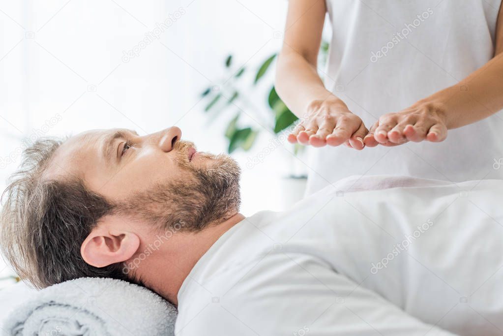 cropped shot of bearded man receiving reiki treatment
