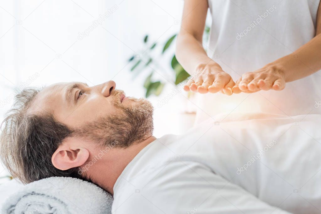 cropped shot of bearded man looking up while receiving reiki treatment