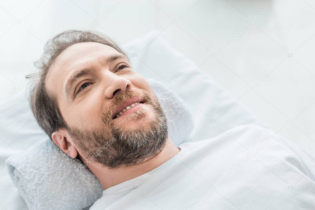 smiling bearded male patient lying on massage table in medical office