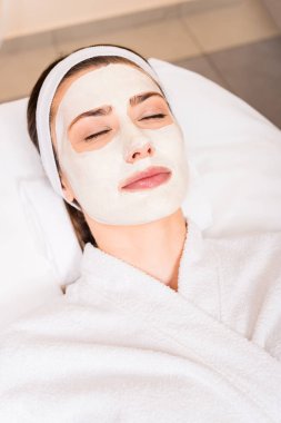 uygulanan yüz maskesi ve kapalı gözler güzellik salonu ile beyaz bornoz içinde yatan kadın