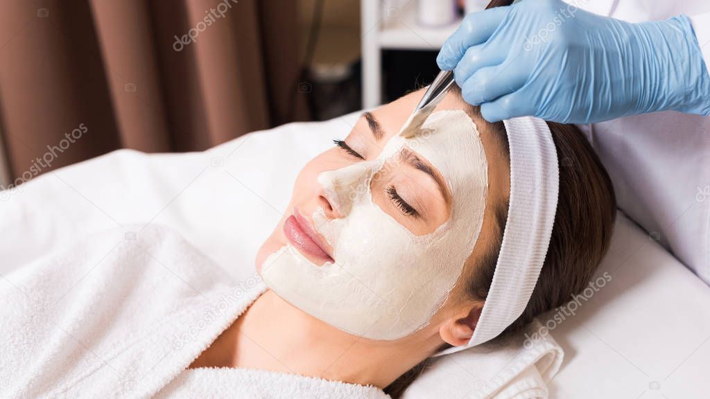 beautician applying cosmetic mask to woman on half  face with cosmetic brush   at beauty salon