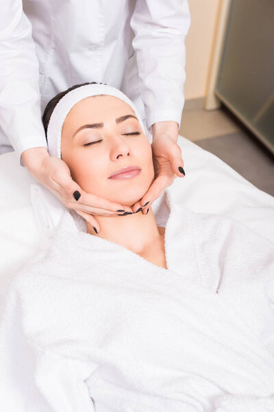 cosmetologist doing manual massage on woman face at beauty salon