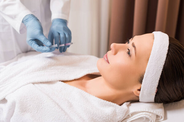 beautician holding syringe near woman at beauty salon