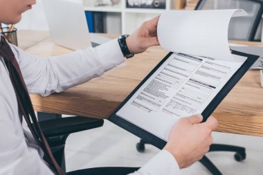 cropped view of businessman reading compensation claim form at office clipart