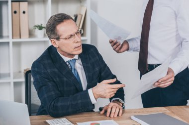 Orta yaşlı işadamı duran ve belgeler Office, tazminat kavramı giving onu cezbetmek işçisi masa oturma