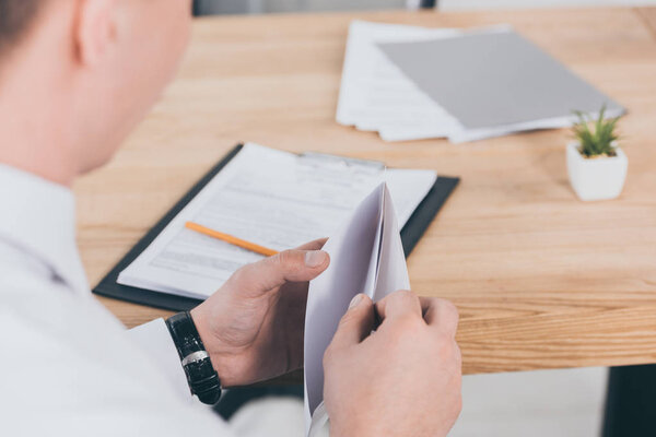 cropped view of businessman opening envelope at workspace, compensation concept