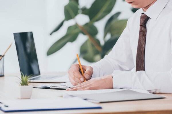 cropped view of businessman writing in document at workplace, compensation concept