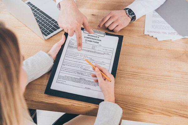 cropped view of businessman pointing with finger at compensation claim form while woman holding pencil and clipboard