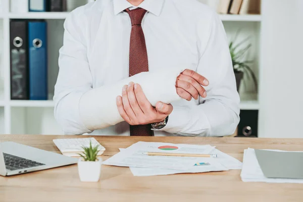 Vista Recortada Del Trabajador Sosteniendo Brazo Roto Wile Sentado Mesa — Foto de Stock