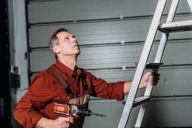 repairman climbing with screwdriver on ladder in garage clipart