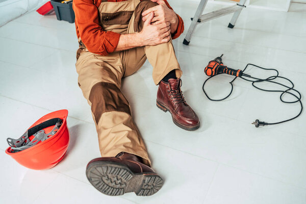 cropped view of repairman sitting on floor and holding injured knee in office