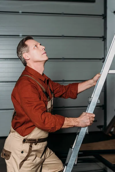 修理工在橙色制服攀爬在梯子上在车库 — 图库照片