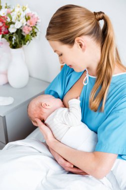 Hastane odasında yatak ve emzirme, Bebek oturan genç anne gülümseyerek, yüksek açılı görünüş