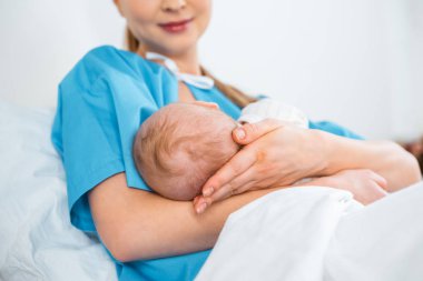 Genç anne emzirme yeni doğan bebek yatakta hastane odasında gülümseyen, düşük açılı görünüş