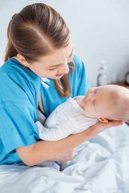 bir hastane yatağında üzerinde oturan ve bebek taşıyan genç anne yüksek açılı görünüş