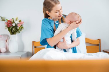 seçici odak bir hastane yatağında şirin yeni doğan bebekle oturan genç anne