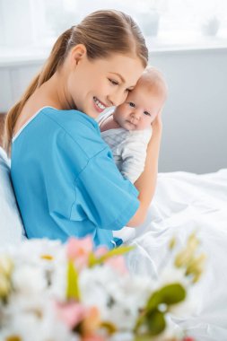 seçici odak bir hastane yatağı üzerinde oturan ve bebek sarılma gülümseyen Genç Anne  