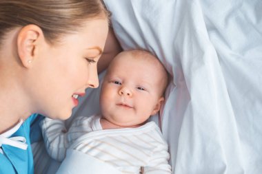 Yeni doğan bebek yatakta yatarken bakarak mutlu genç anne