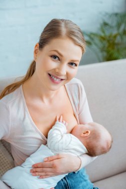 mutlu genç anne emzirme bebek ve kameraya gülümseyen