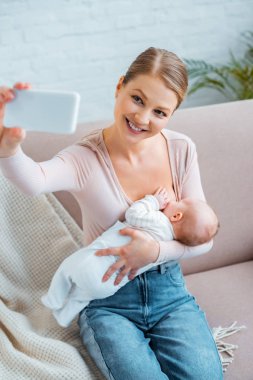 mutlu genç kadın anne sütü bebek ve alma selfie ile smartphone evde yüksek açılı görünüş
