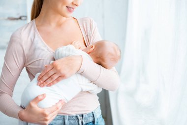 Genç Anne ayakta ve emzirme bebek bebek evde gülen in kırpılmış atış