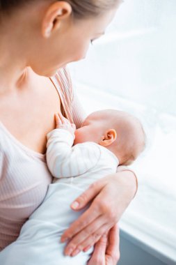 cropped shot of young mother breastfeeding adorable baby at home clipart