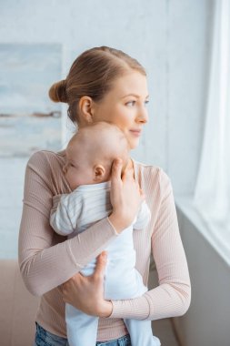 güzel genç anne bebek tutan ve penceresine bakarak