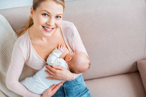 high angle view of happy young mother breastfeeding baby and smiling at camera