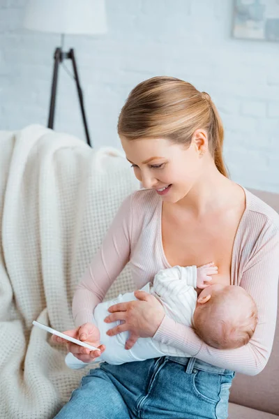 幸せな若い母親母乳赤ちゃんと家でスマート フォンを使用しての高角度のビュー — ストック写真