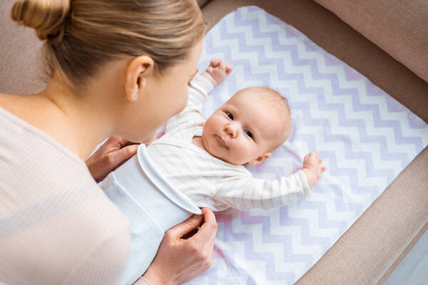 high angle view of mother putting clothes on adorable infant baby