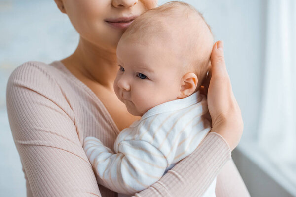 cropped shot of happy mother holding adorable baby at home