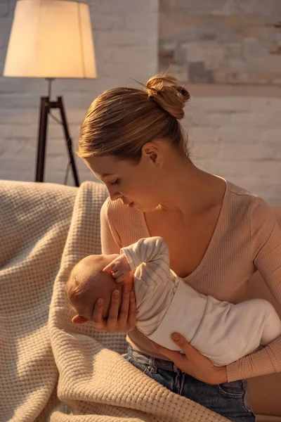 年轻的母亲坐在沙发上 晚上母乳喂养时抱着新生儿 — 图库照片