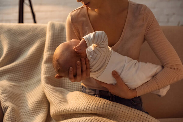 cropped shot of young mother holding baby during breastfeeding at night