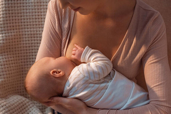 cropped shot of young mother breastfeeding baby at night