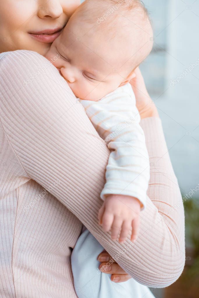 cropped shot of happy young mother carrying adorable sleeping baby 