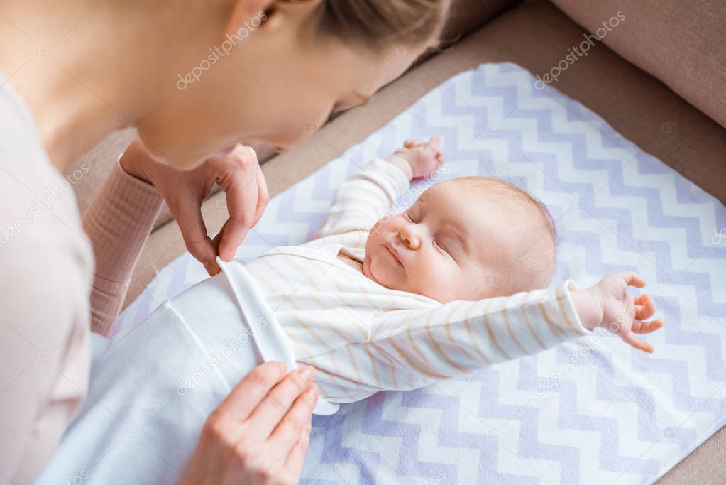 cropped shot of mother putting clothes on adorable infant baby lying on sofa 