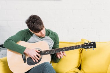 sarı koltukta oturan ve akustik gitar çalmak genç adam