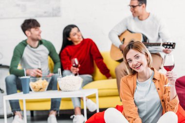 şarap tutarak ve çok kültürlü arkadaşlar sarı kanepede rahatlatıcı süre kamera bakıyor güzel kız 