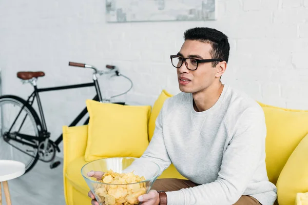 Joven Hombre Raza Mixta Sentado Sofá Amarillo Sosteniendo Tazón Patatas —  Fotos de Stock