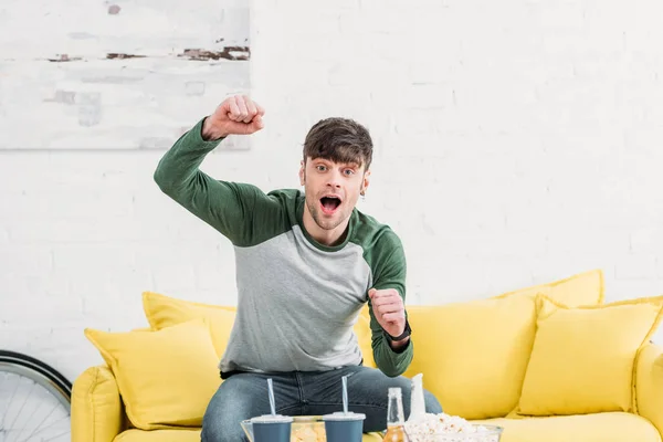 Joven Emocionado Sentado Sofá Amarillo Viendo Partido Deportivo — Foto de Stock